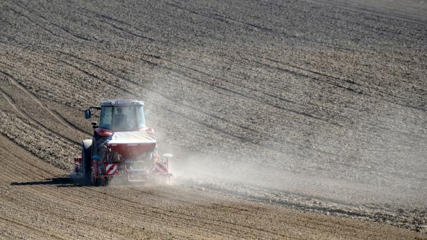 Ein Traktor bearbeitet ein großes Feld, Staub wirbelt auf.