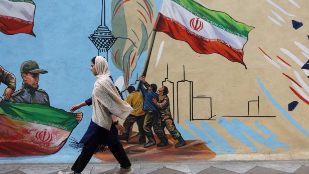An Iranian woman walks next to a mural on a street in Tehran