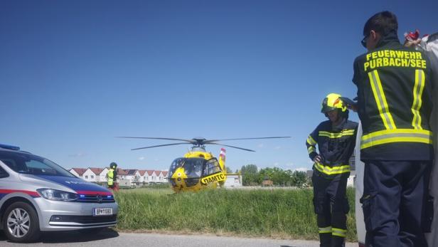 Ein gelber Rettungshubschrauber landet neben einer Straße, Feuerwehrleute und ein Polizeiauto sind vor Ort.