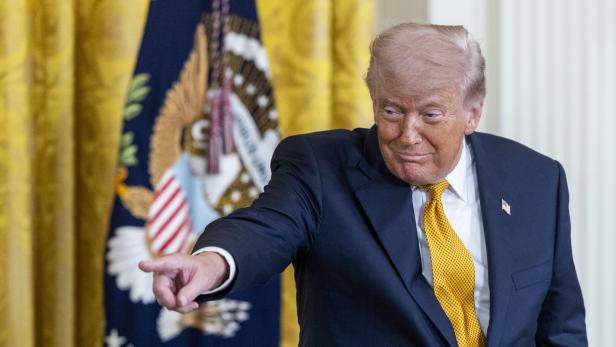 Donald Trump zeigt mit dem Finger vor einem Hintergrund mit dem US-Präsidenten-Siegel.