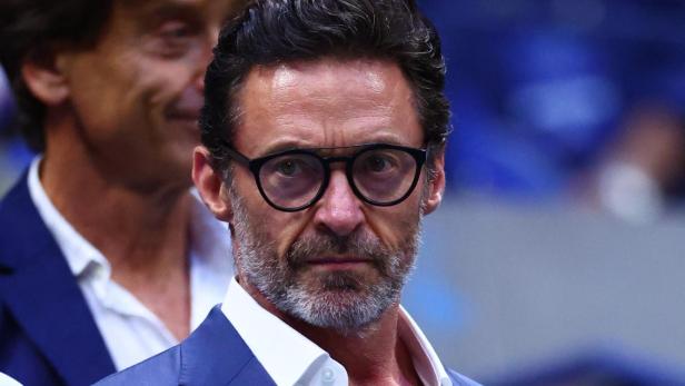 Hugh Jackman mit Brille und blauem Anzug blickt ernst in die Kamera.