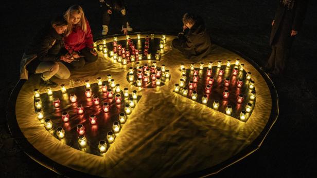 Menschen zünden Kerzen auf einem großen gelben Symbol für Radioaktivität an, das aus vielen kleinen Lichtern besteht.