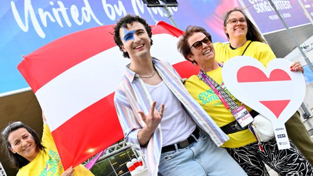 Vier fröhliche Menschen mit Österreich-Flagge und Herzsymbol feiern vor einem Eurovision Song Contest Plakat.