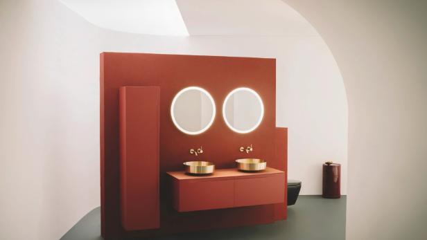 Modernes Badezimmer mit rotbrauner Wand, zwei runden Spiegeln und goldenen Waschbecken.