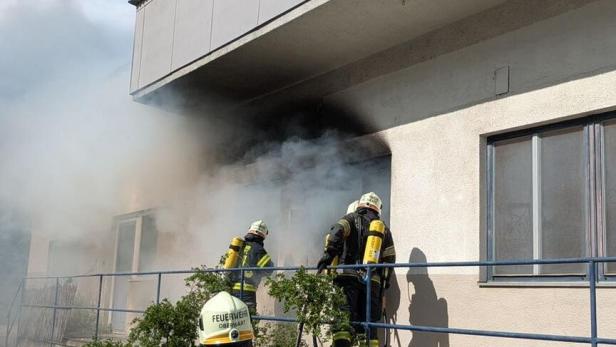 Drei Feuerwehrleute mit Atemschutzgeräten bekämpfen einen Brand in einem verrauchten Gebäude.