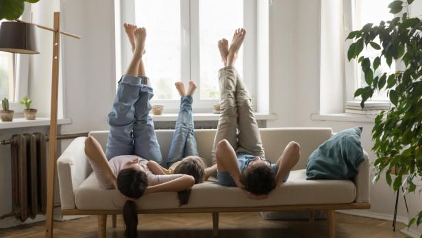 Zwei Menschen liegen lachend kopfüber auf einem Sofa, halten Händchen und strecken die Beine in bunten Socken nach oben.