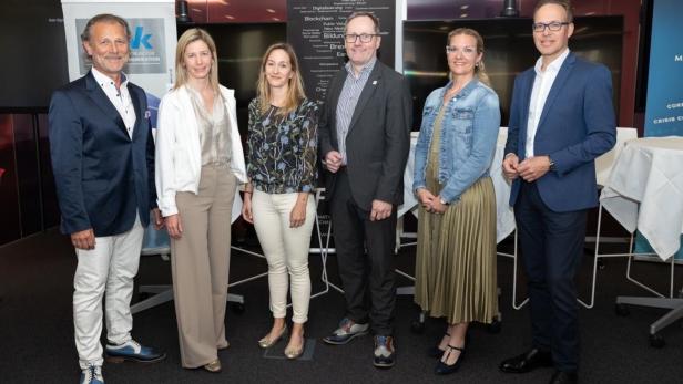 Sechs Personen stehen nebeneinander in Businesskleidung und lächeln in einer modernen Konferenzumgebung.