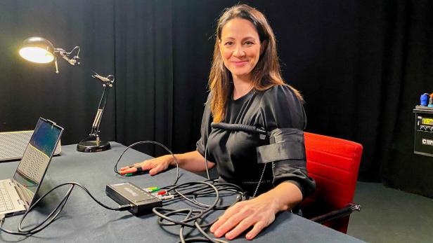 Lisa Gadenstätter sitzt mit Polygraphen-Sensoren an Fingern und Arm an einem Tisch mit Laptop.