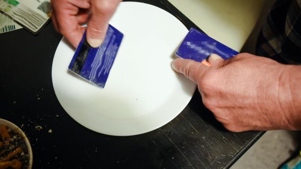 Zu sehen sind zwei Hände, die mit Plastikkarten ein Rauschgift-Pulver portionieren