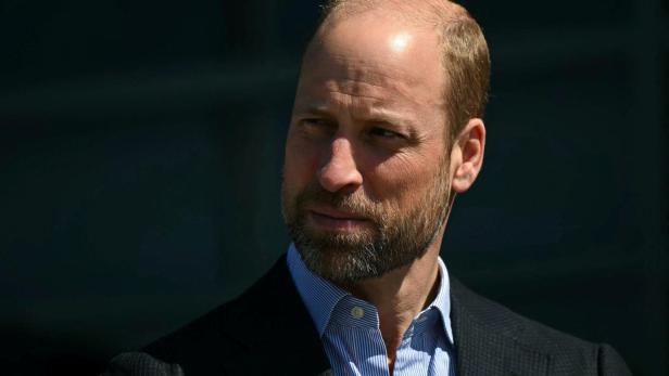 Prinz William mit Bart und blau gestreiftem Hemd blickt zur Seite.