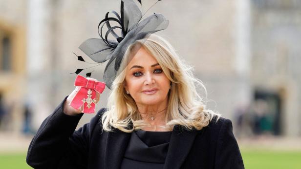 Eine blonde Bonnie Tyler mit Hut hält eine Auszeichnung mit roter Schleife in der Hand.