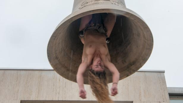 Die nackte Künstlerin Florentina Holzinger hängt kopfüber, als menschlicher Schlegel, in einer großen Messingglocke 