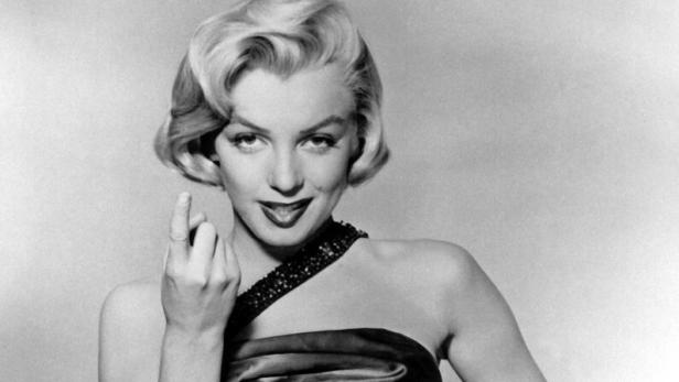 Marilyn Monroe im schwarzen Abendkleid mit neckischem Blick und erhobenem Finger.
