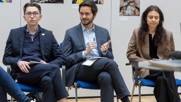 Drei junge Erwachsene in Businesskleidung sitzen nebeneinander und diskutieren in einem modernen Raum.