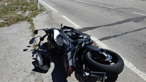 Ein Motorrad liegt umgestürzt am Straßenrand, daneben ein beschädigter Helm und ein Rettungswagen steht weiter vorne.