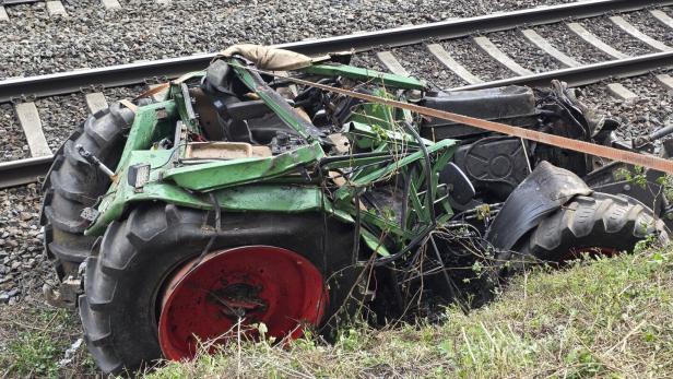 Ein zerstörter, grüner Traktor liegt neben Bahngleisen im Gras.