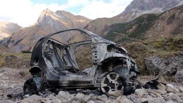 Ein ausgebranntes Auto steht in einer felsigen Berglandschaft.