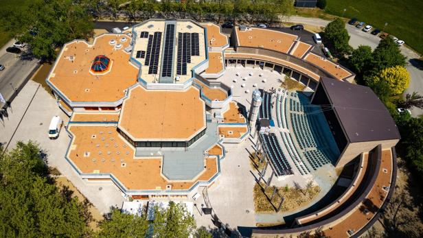 Luftaufnahme eines Gebäudes mit orangefarbenem Dach, Solarmodulen und einem Amphitheater.