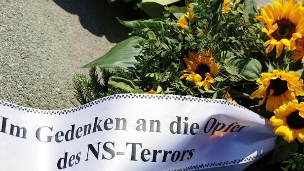 Ein Kranz mit Sonnenblumen und der Aufschrift "Im Gedenken an die Opfer des NS-Terrors" liegt auf dem Boden.
