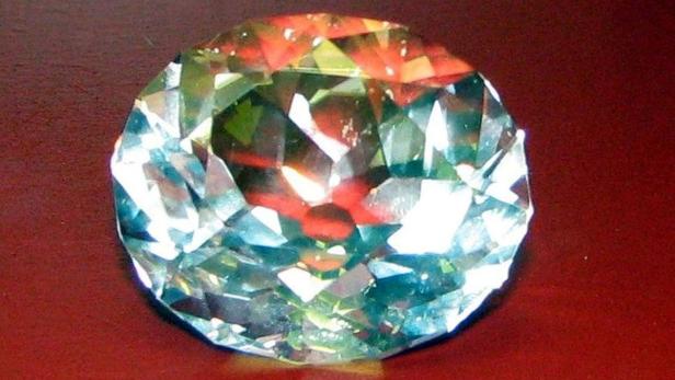 Ein großer, geschliffener Diamant liegt auf einer roten Oberfläche.