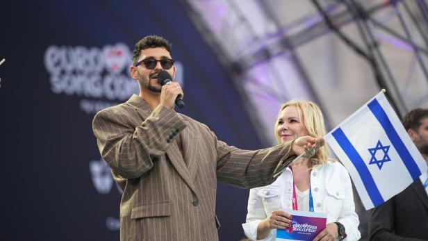 Ein Mann mit Mikrofon und Sonnenbrille steht neben einer Frau, die eine israelische Flagge hält, auf einer Bühne beim Eurovision Song Contest.