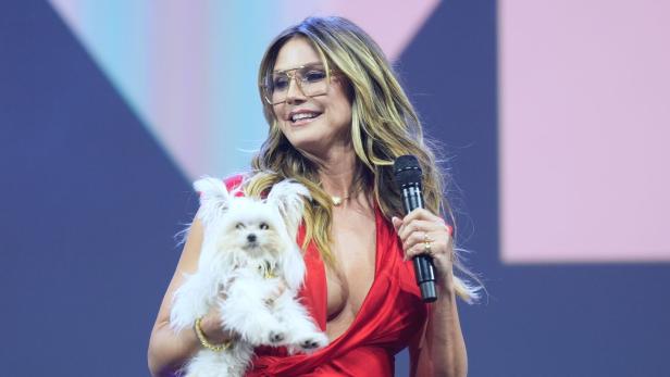 Heidi Klum hält einen kleinen, weißen Hund und ein Mikrofon in der Hand.