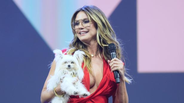 Heidi Klum hält einen kleinen, weißen Hund und ein Mikrofon in der Hand.
