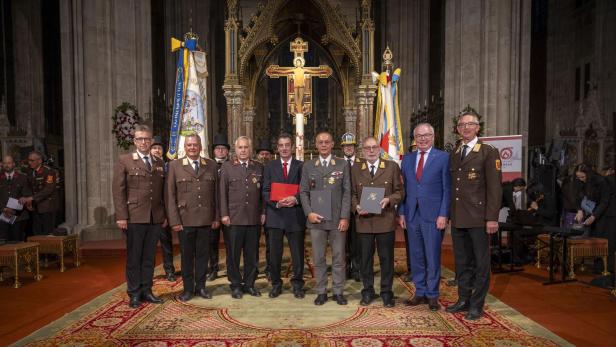 Mehrere Männer in Feuerwehruniform und Anzug posieren mit Urkunden in einer Kirche.