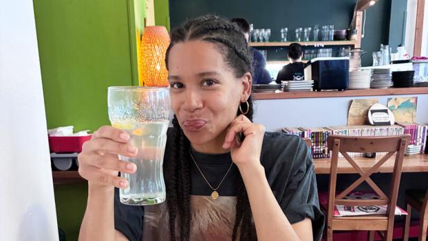 Rebecca Horner sitzt an einem Tisch, vor sich asiatische Speisen, in der Hand ein großes Glas Soda-Zitron