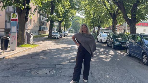 Eine Frau steht auf einer von Bäumen gesäumten Straße, umgeben von geparkten Autos und Sonnenschein.