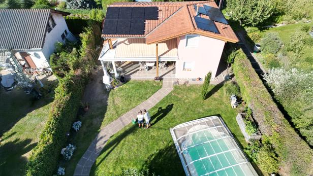 Haus mit Photovoltaikanlage auf dem Dach, Garten und überdachtem Pool bei Sonnenschein.