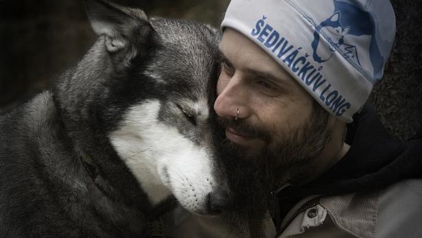 Ein Mann mit Mütze kuschelt eng mit einem Husky, beide wirken entspannt und verbunden.
