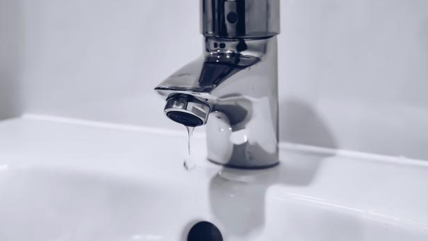 Einzelner Wassertropfen tropft aus einem Wasserhahn in ein weißes Waschbecken.