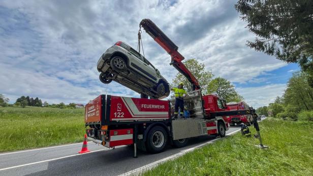 Ein Feuerwehrkran hebt ein Auto von der Straße, während Einsatzkräfte daneben stehen.