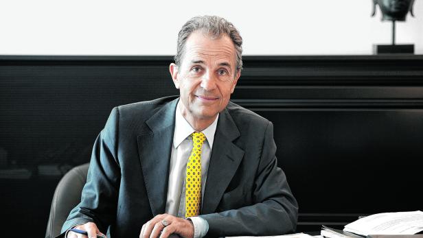 Ein Mann im Anzug sitzt an einem Schreibtisch mit einer Buddha-Statue im Hintergrund.