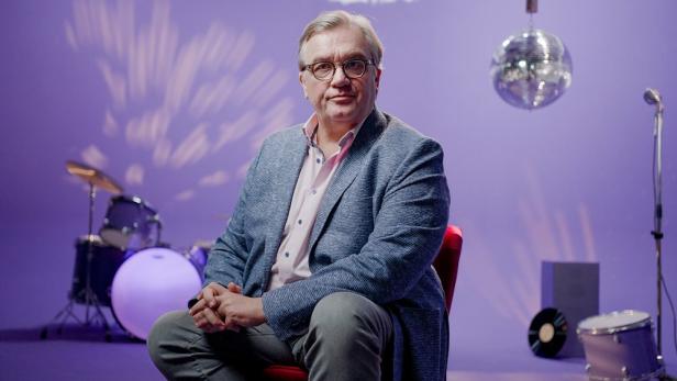 Hape Kerkeling sitzt in TV-Studio vor Schlagzeug und Mikroständer unter Discokugel