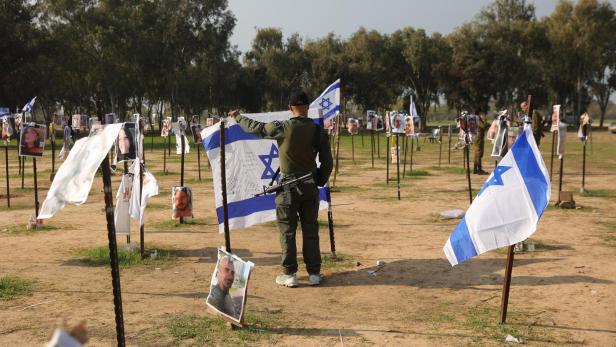 Ein Soldat steht auf einem Feld mit israelischen Flaggen und Fotos von Menschen.