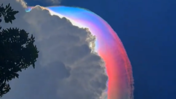 Eine große Wolke mit leuchtenden Regenbogenfarben am Himmel vor blauem Hintergrund.