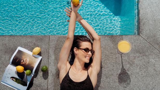 Eine Frau liegt lächelnd am Pool 