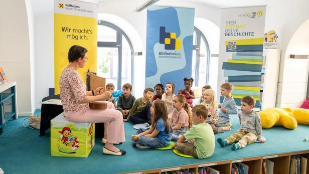 Eine Frau liest einer Gruppe von Kindern in einer Bibliothek vor.