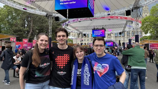 Vier Freunde posieren vor einer Bühne des Eurovision Song Contest in Wien.