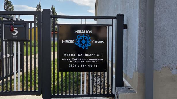 Schwarzes Firmenschild von „Miralios Magic Cards“ an einem modernen Metalltor vor einem Wohnhau