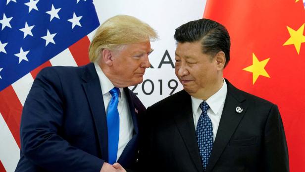 Donald Trump und Xi Jinping schütteln sich vor den Flaggen der USA und Chinas die Hände.