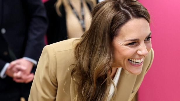Prinzessin Kate lacht in einem beigen Hosenanzug, leicht nach vorne gebeugt.