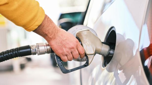 Hand hält Zapfpistole und tankt ein Auto an einer Tankstelle.