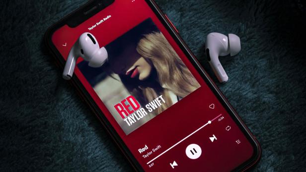 Smartphone mit Spotify-App zeigt das Album "Red" von Taylor Swift und zwei kabellose Kopfhörer.
