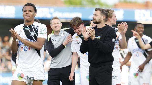 Eine Gruppe von SK Sturm Graz Spielern und Trainern applaudiert auf dem Rasen.