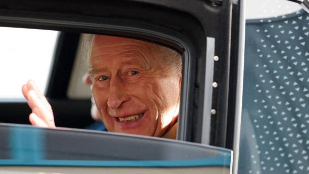 König Charles III. lächelt aus einem Autofenster und winkt.