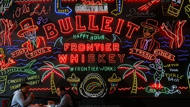 People eat in front of a sign for Bulleit Frontier Whiskey in Grand Central Market in Los Angeles
