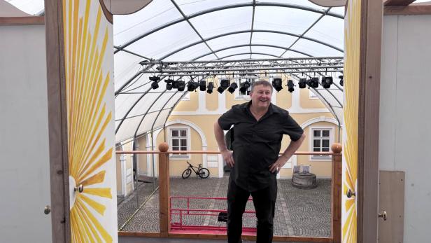 Ein Mann steht auf einer überdachten Theaterbühne mit gelbem Bühnenbild und Blick nach draußen.